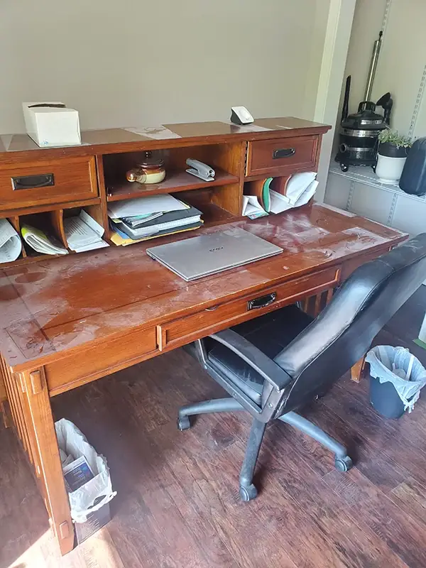 Wooden desk with a dull, streaky and spotted surface and clutter underneath