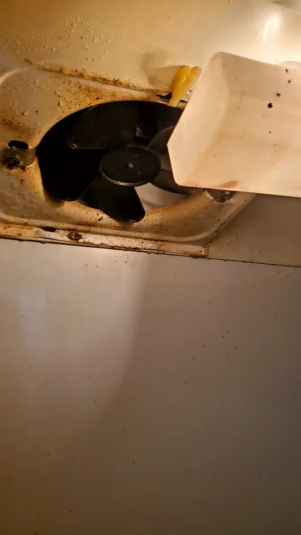 Range hood vent with a grease-coated fan, rusty edges and a stained cover