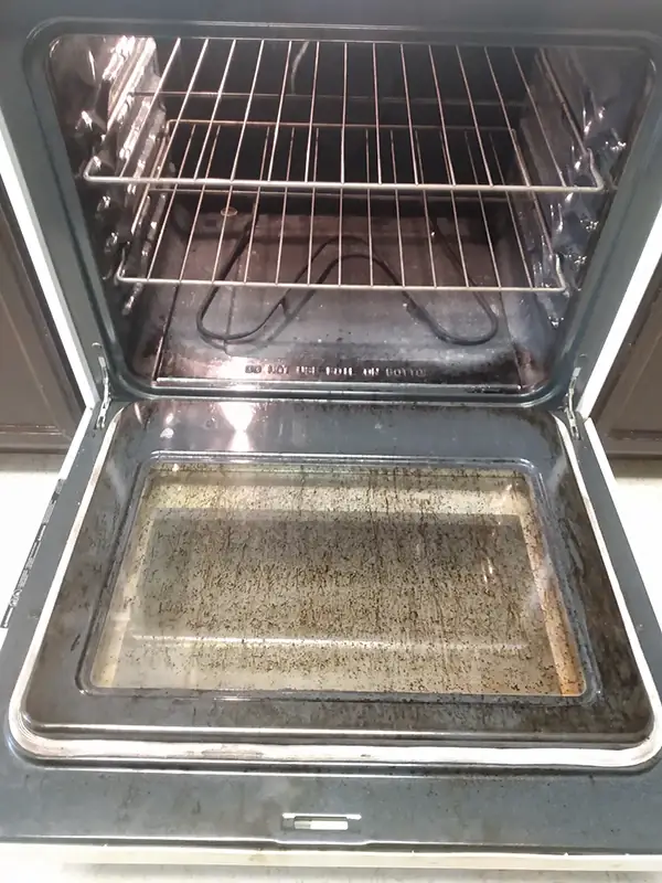 Open oven door with the glass covered in baked-on grease and dark splatter