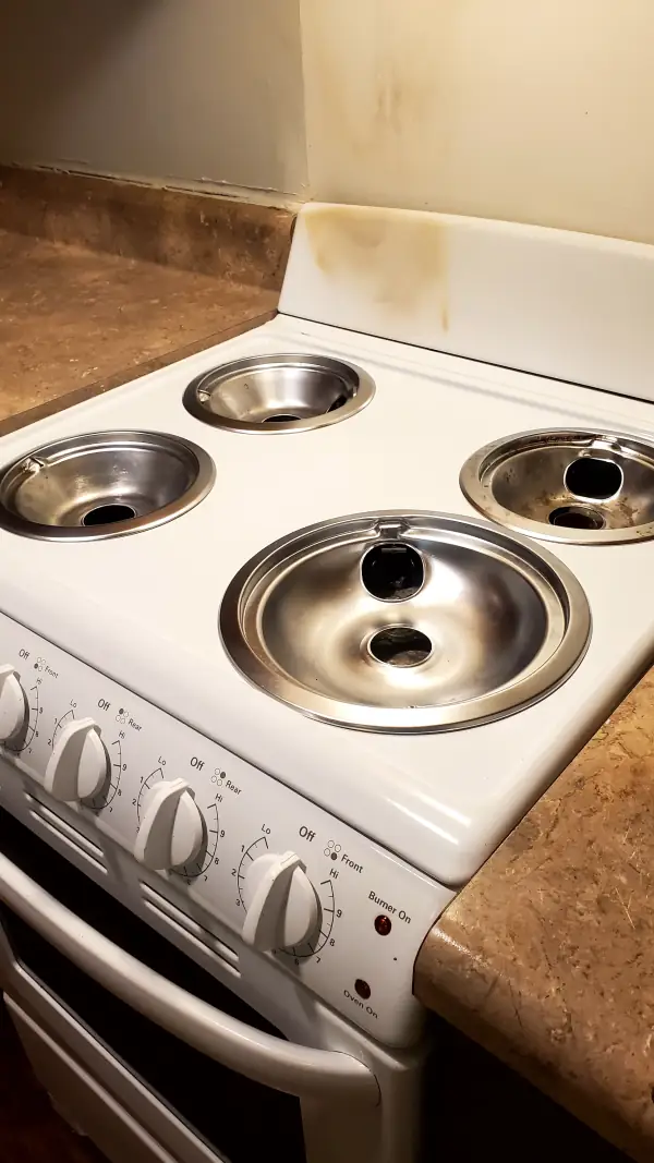 The same stovetop with shiny drip pans, clean burners and a wiped-down backsplash