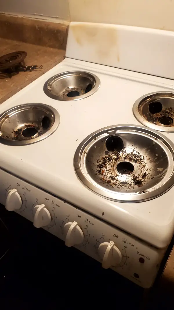 Electric stovetop with burnt food caked in the drip pans and grease stains on the backsplash